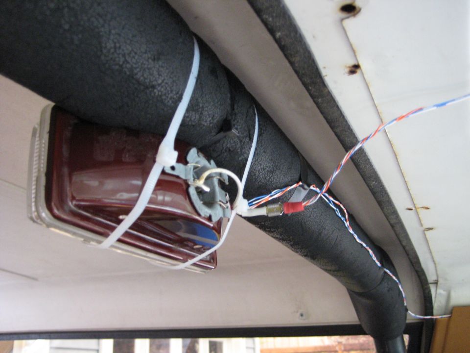 Maroon taillight assembly with wires attached, secured by zip ties to a black insulated tube.