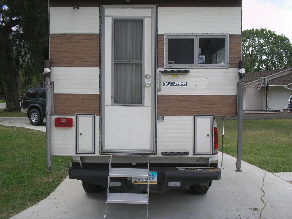 Rear view of a truck camper with brown and white stripes, a door, and windows.