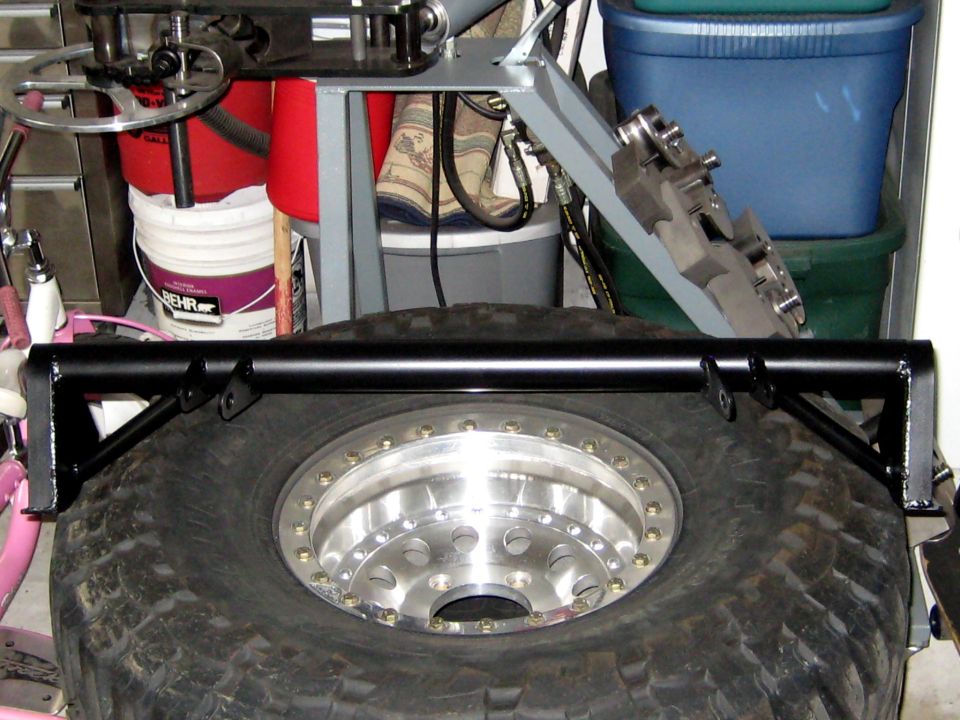 Black swing-away tire carrier mounted on a spare tire with a silver beadlock wheel.