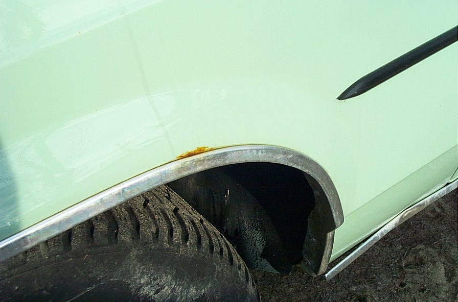 Close-up of a light green car's fender, showing a tire and some rust around the wheel well