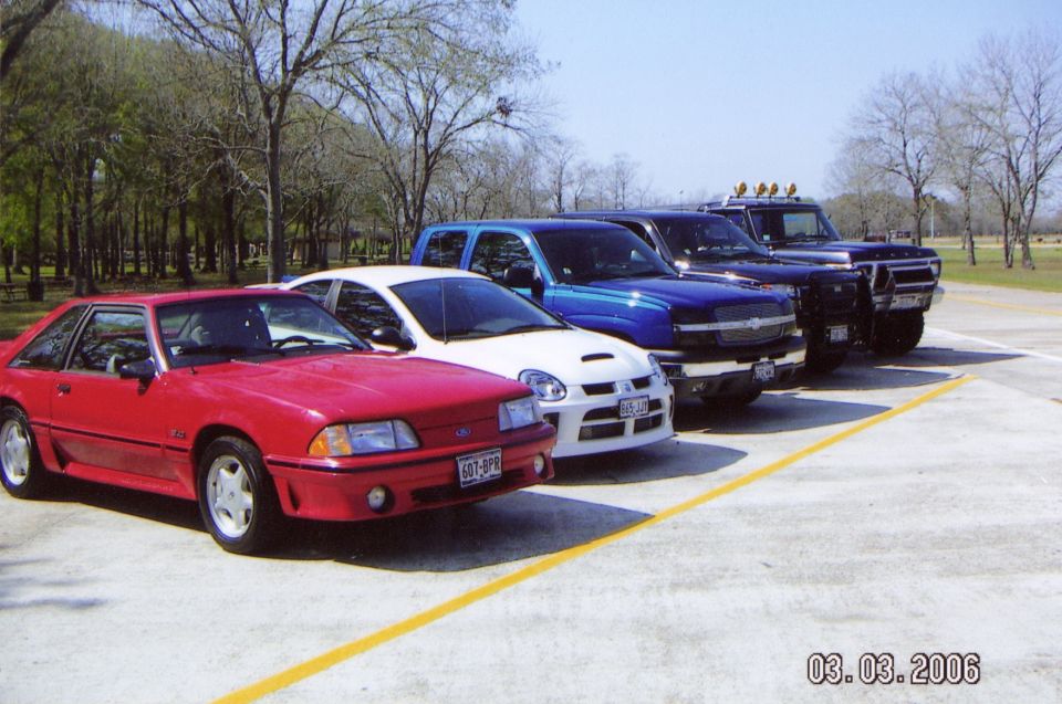 Red coupe, white sedan, blue pickup truck, and dark blue SUV parked in a line.