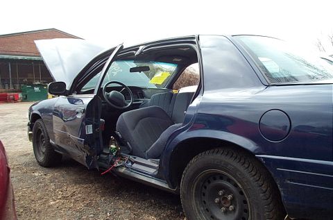 2001 Ford Crown Victoria - A dark blue 2001 Ford Crown Victoria is shown with its hood and driver's door open, revealing interior damage and exterior dents.