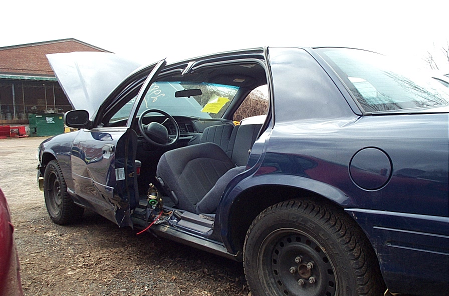 Dark blue 2001 Ford Crown Victoria with hood and driver's door open, showing interior and damage to the driver's side