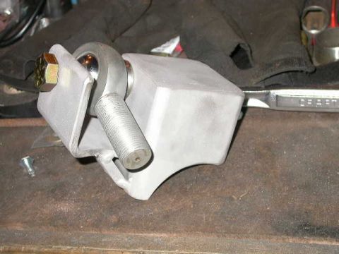 1990 Ford Bronco - A close-up view of a custom fabricated metal bracket with a spherical bearing and a bolt assembly, resting on a workbench. A wrench is visi…