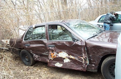 2001 Ford Crown Victoria - A severely damaged brown sedan sits in an outdoor lot with another vehicle nearby.