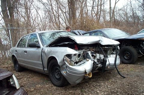 2001 Ford Crown Victoria - A severely damaged 2001 Ford Crown Victoria sits in a lot with its hood crumpled and front end destroyed.