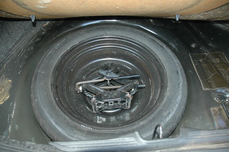 Spare tire in trunk well with scissor jack and tools stored in center.