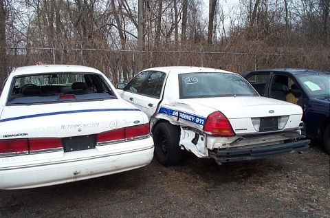 2001 Ford Crown Victoria - Two damaged police Crown Victorias are parked side-by-side in an outdoor lot.