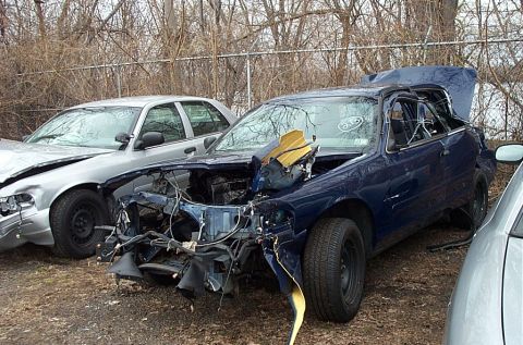2001 Ford Crown Victoria - Two damaged sedans are parked outdoors, with the blue car showing significant front-end destruction.