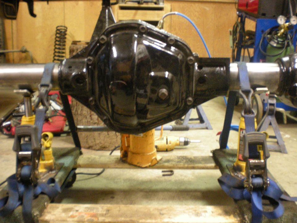 Black solid axle housing strapped to bench over bottle jack during setup work