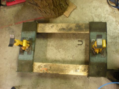 1993 Ford Bronco - A wooden frame with two yellow hydraulic jacks is positioned on a concrete floor, with a large log in the background.