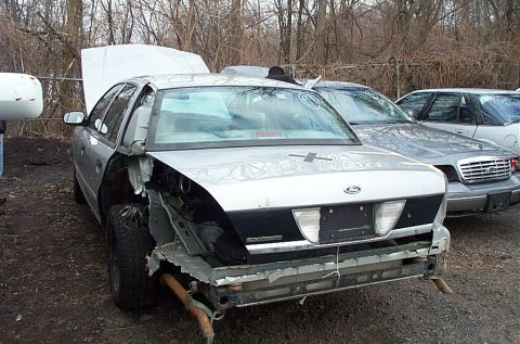 2001 Ford Crown Victoria - A severely damaged 2001 Ford Crown Victoria sits in a junkyard next to another similar vehicle.