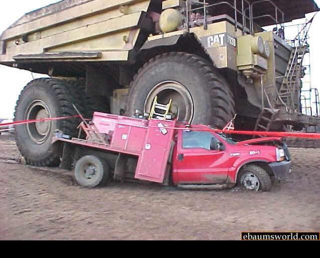 Red truck stuck under a giant yellow mining truck