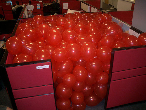 Office cubicle filled with red balloons
