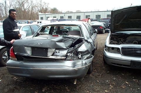 2001 Ford Crown Victoria - A heavily damaged 2001 Ford Crown Victoria sits in a lot next to another vehicle.