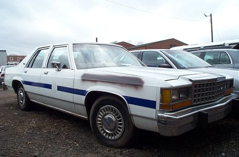 2001 Ford Crown Victoria - This white sedan with a blue stripe is parked outdoors. The vehicle's front grille and body style suggest an older model, likely from the 1…
