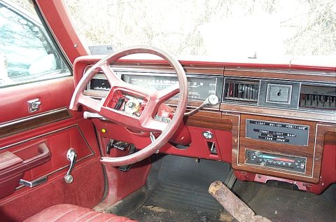 2001 Ford Crown Victoria - The interior of a car shows a red dashboard with wood grain accents and a manual window crank.