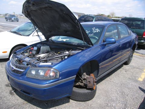 2001 Ford Crown Victoria - Blue sedan with hood open and missing front wheel, parked outdoors.