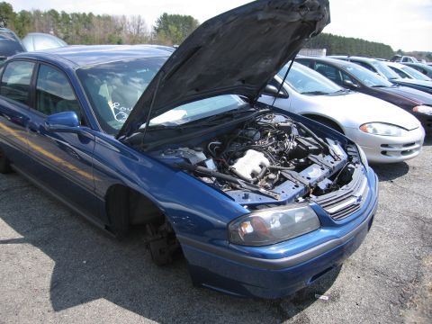 2001 Ford Crown Victoria - A blue sedan sits in a lot with its hood open, revealing the engine compartment and missing front wheel.