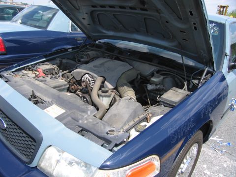 2001 Ford Crown Victoria - The engine bay of a 2001 Ford Crown Victoria is shown, with another similar vehicle visible in the background.