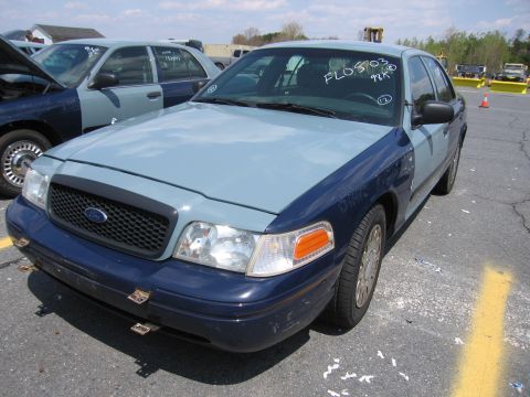 2001 Ford Crown Victoria - A two-tone Ford Crown Victoria is parked in an outdoor lot with another vehicle visible.
