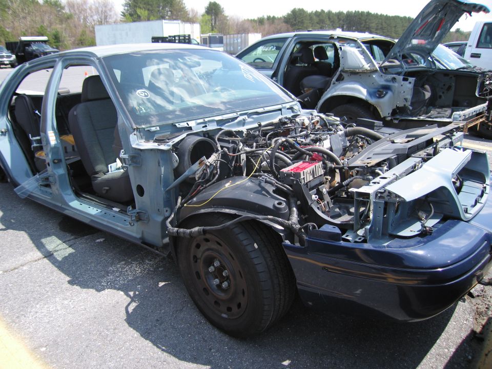 Blue 2001 Ford Crown Victoria stripped of body panels, showing engine and interior, parked in a lot