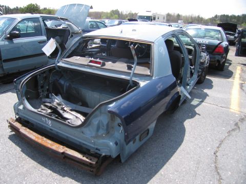 2001 Ford Crown Victoria - Junkyard scene shows a stripped 2001 Ford Crown Victoria police car with its trunk open.