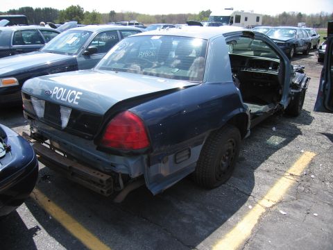2001 Ford Crown Victoria - This damaged police car is missing its doors and appears to be in a salvage yard with other vehicles.