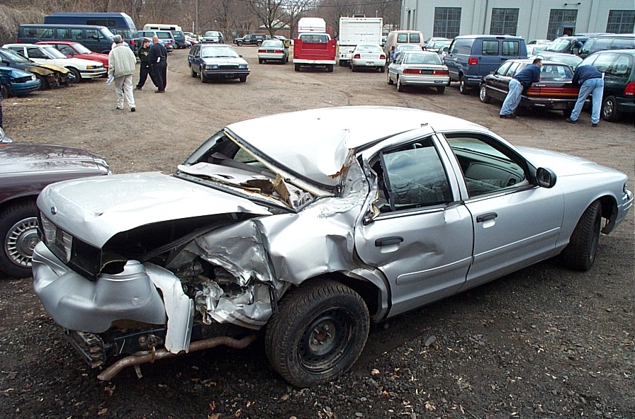 2001 Ford Crown Victoria with severe rear and front damage, parked in a lot with other vehicles