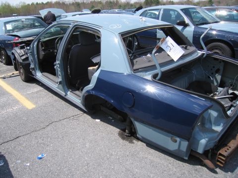 2001 Ford Crown Victoria - A damaged car sits in a lot, with another similar vehicle visible behind it.