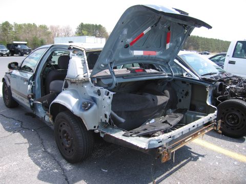 2001 Ford Crown Victoria - A damaged 2001 Ford Crown Victoria sits in a lot with its trunk open and rear quarter panel removed.