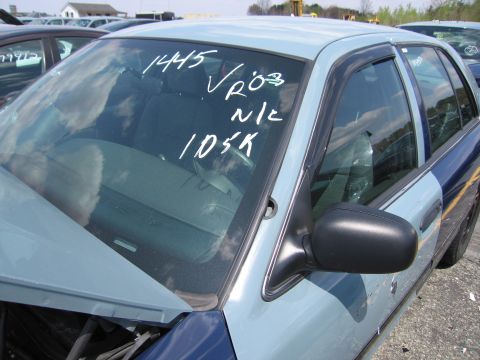 2001 Ford Crown Victoria - A two-tone police car sits in a lot with other vehicles, its windshield marked with white writing.