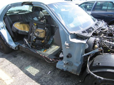 2001 Ford Crown Victoria - A damaged 2001 Ford Crown Victoria sits in a junkyard, its interior and engine compartment exposed.