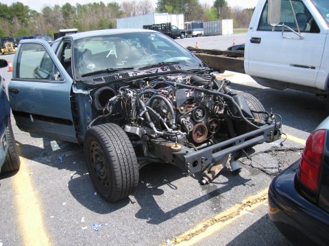 2001 Ford Crown Victoria - A dismantled blue sedan sits in a lot, its engine exposed and front end removed.