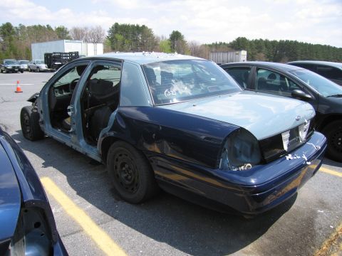2001 Ford Crown Victoria - A heavily damaged 2001 Ford Crown Victoria sits in a parking lot, stripped of its doors and body panels.