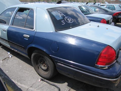 2001 Ford Crown Victoria - Rear view of a two-tone 2001 Ford Crown Victoria in a junkyard with other cars visible.