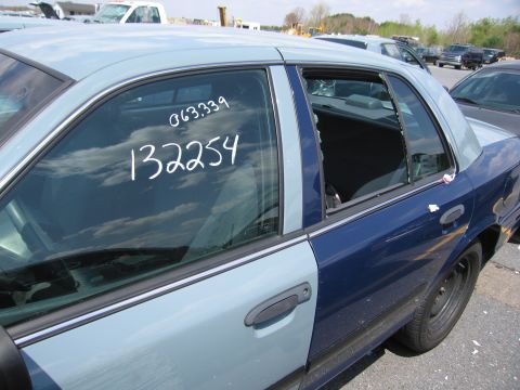 2001 Ford Crown Victoria - A damaged sedan with two-tone paint and handwritten numbers on the window sits in a junkyard.
