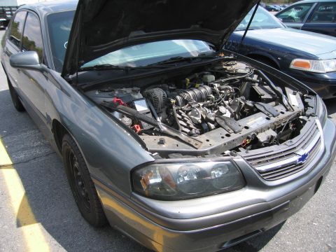 2001 Ford Crown Victoria - The front of a gray Chevrolet sedan is shown with its hood open, revealing the engine compartment.