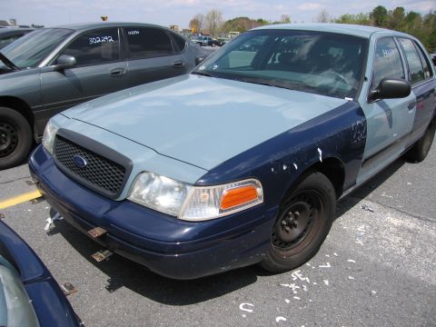 2001 Ford Crown Victoria - A two-tone Ford Crown Victoria is parked in a lot with another vehicle nearby.