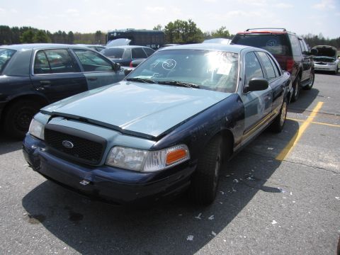 2001 Ford Crown Victoria - A two-tone Ford Crown Victoria is parked in a lot with other vehicles, its hood ajar.