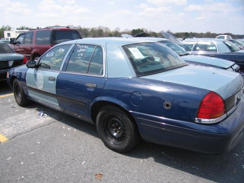 2001 Ford Crown Victoria - This two-tone blue sedan has a bullet hole on the rear fender and appears to be in a vehicle lot.