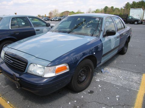 2001 Ford Crown Victoria - Two Ford Crown Victoria police cars parked in a lot, one with visible auction markings on the windshield.