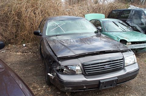 2001 Ford Crown Victoria - A damaged 2001 Ford Crown Victoria sits in a junkyard with other vehicles.
