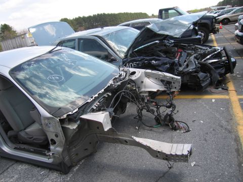 2001 Ford Crown Victoria - Two severely damaged vehicles are parked in a lot, with one showing significant front-end destruction.