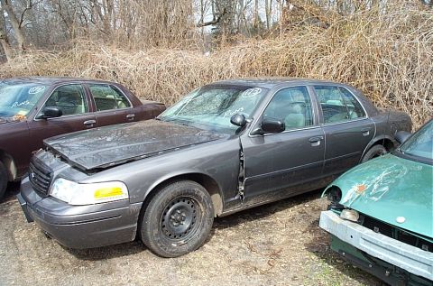 2001 Ford Crown Victoria - Three cars are parked in an outdoor lot with dry brush in the background. One car's hood is open.