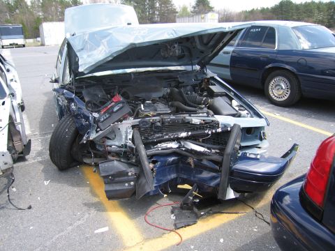 2001 Ford Crown Victoria - Front view of a severely damaged 2001 Ford Crown Victoria, with another police-style Crown Victoria in the background.