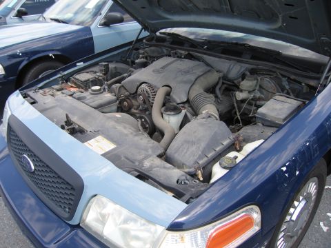 2001 Ford Crown Victoria - The engine bay of a 2001 Ford Crown Victoria is visible, with another similar vehicle parked alongside.