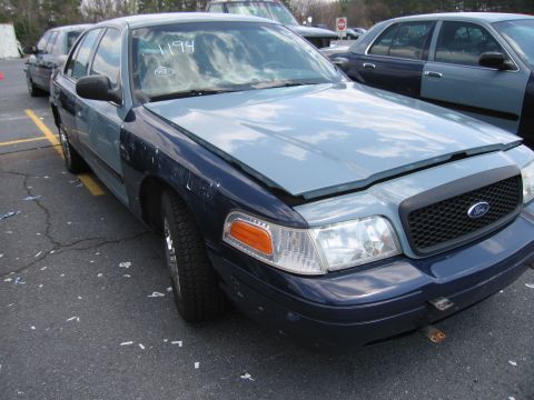 2001 Ford Crown Victoria - A two-tone Ford Crown Victoria is seen from the front with its hood open, parked in a lot with other vehicles.