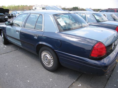 2001 Ford Crown Victoria - A two-tone blue Ford Crown Victoria is parked in a lot with other vehicles, showing its rear passenger side.