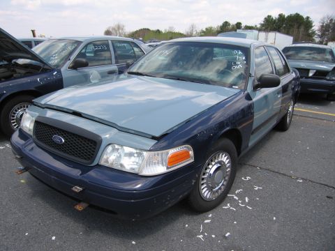 2001 Ford Crown Victoria - A two-tone Ford Crown Victoria sits in a lot with its hood ajar, alongside other vehicles.